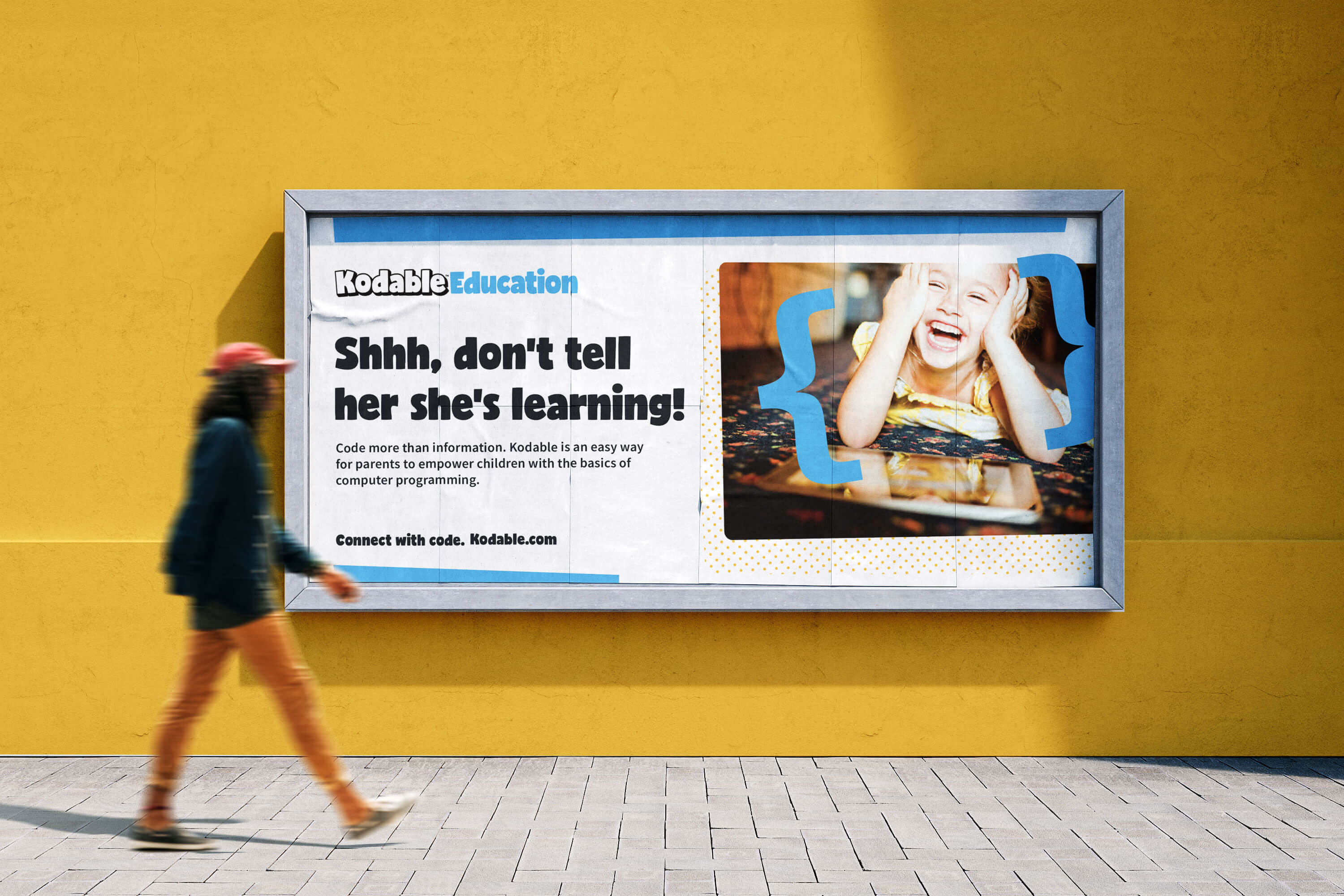 woman walking in front of a yellow wall with an ad for kodable